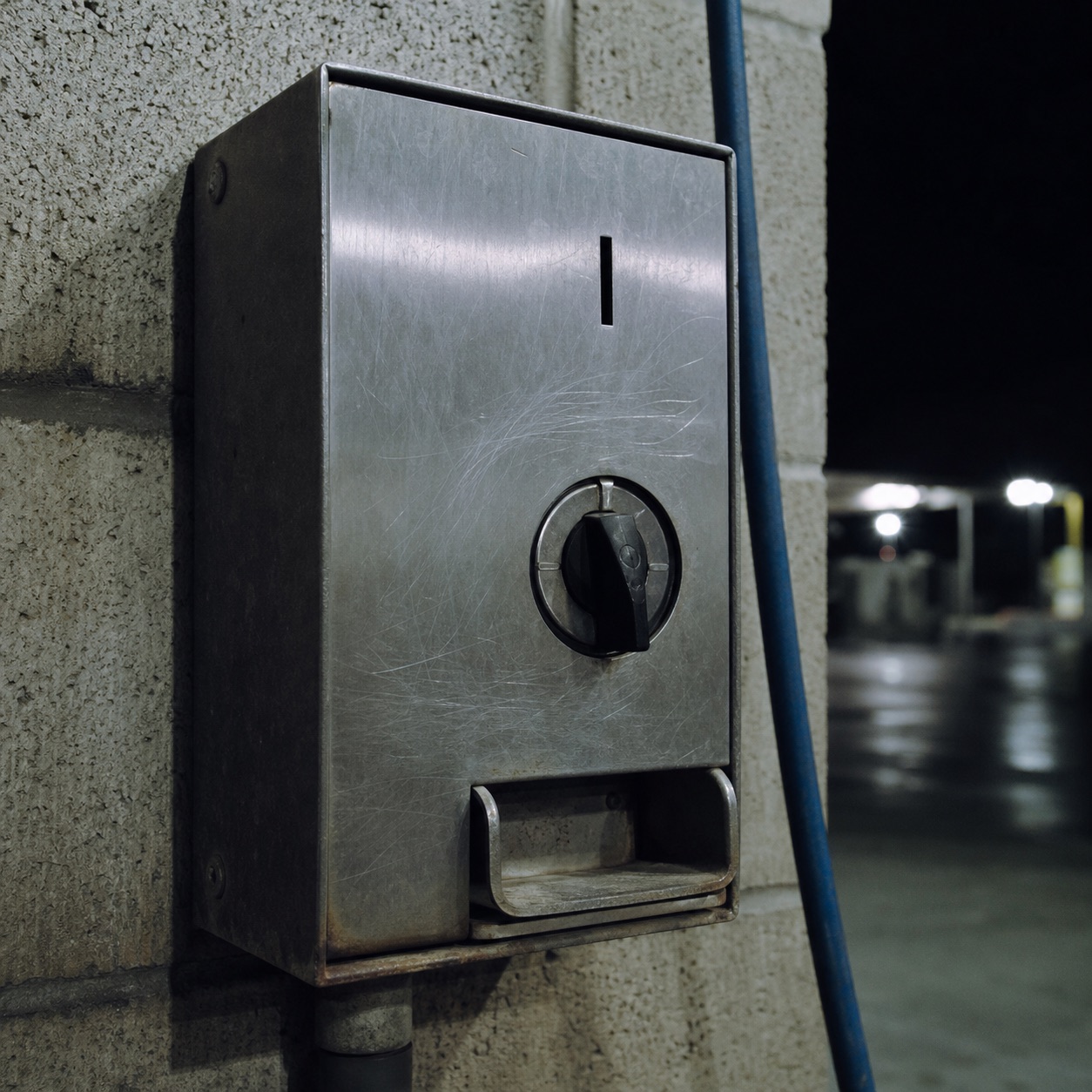 A worn coin-operated timer box on the concrete wall of a car wash bay, lit by fluorescent light.