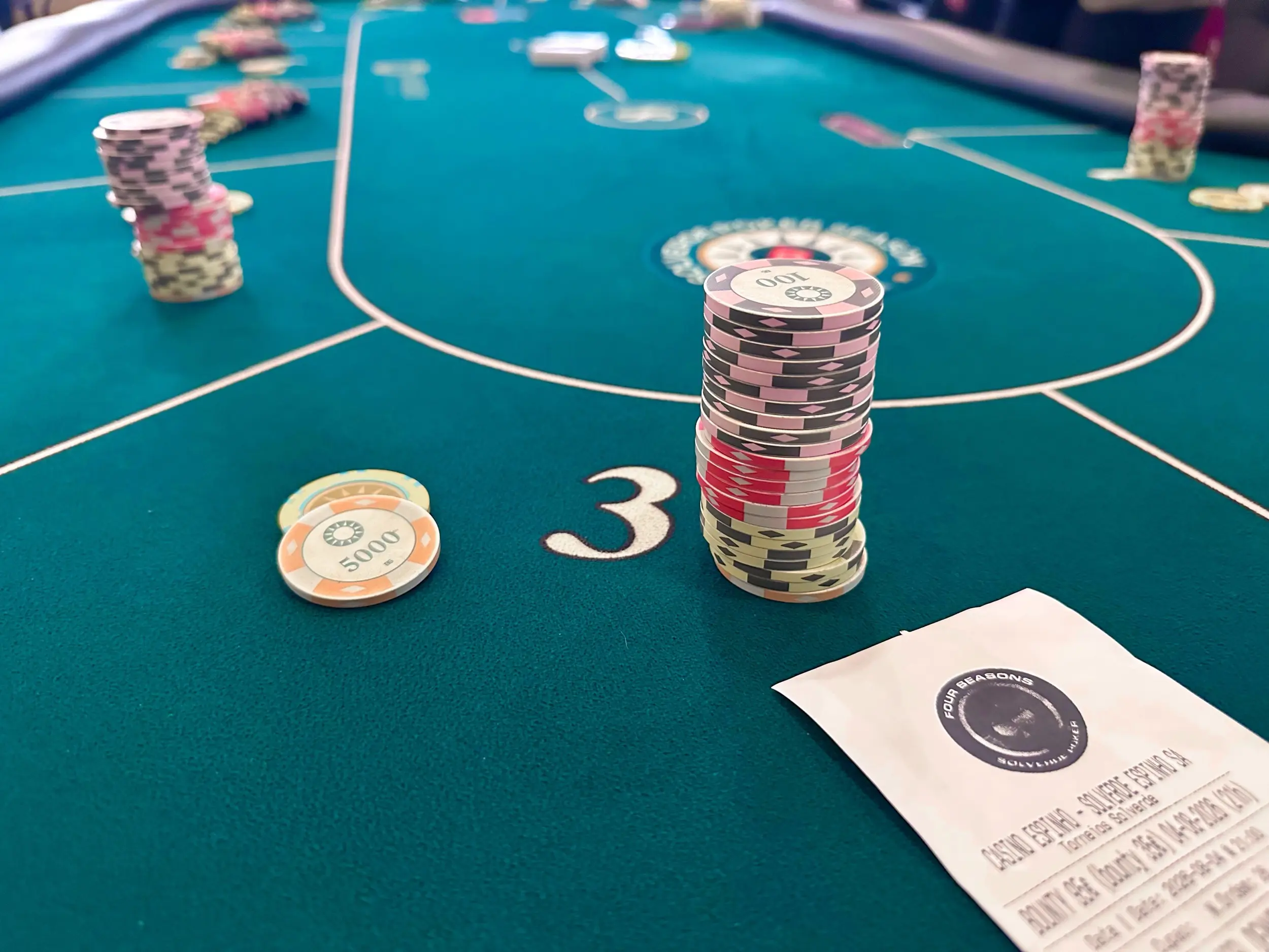 Stacks of pink, black, red, and cream poker chips on a green felt table at Casino Espinho with a Solverde Four Seasons poker slip in the corner
