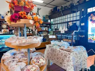 Interior of Dutch Maid Bakery & Cafe decorated with orange and burgundy leaves, flowers, and pumpkins, with tiered wooden displays of wrapped baked goods among antique cabinets and clocks