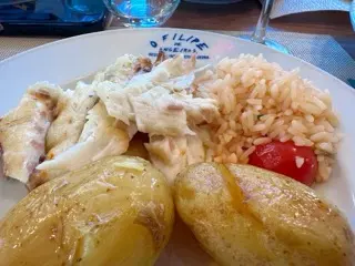 A plate at O Filipe de Angeiras with flaked grilled white fish, tomato rice, and two roasted potatoes, with water glasses and a wine glass on the table