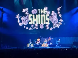 The Shins performing beneath a large blue stage projection filled with illustrated fruit and the band's name at Bridgestone Arena