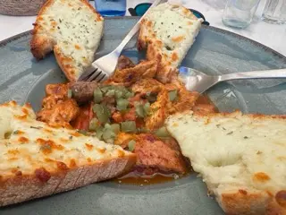 A plate of pica pau in Matosinhos with saucy meat, chopped pickles, and four slices of toast covered in melted cheese around the edge of a gray plate