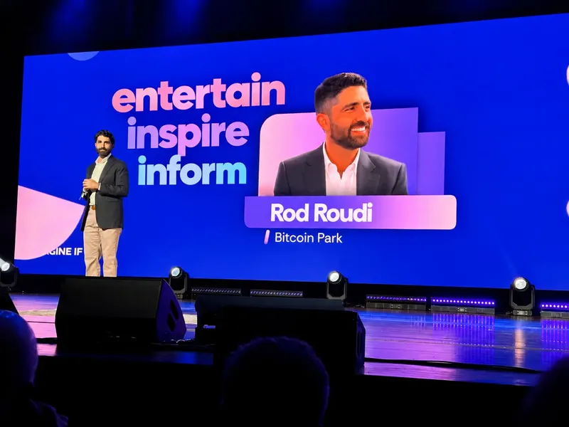 Rod Roudi of Bitcoin Park on stage at the Fisher Center, in front of a screen reading entertain, inspire, inform