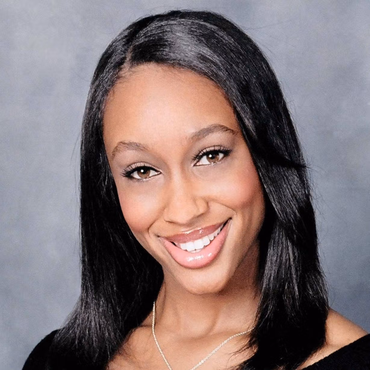 Studio portrait of Mitrice Richardson smiling, wearing a necklace, in front of a gray backdrop